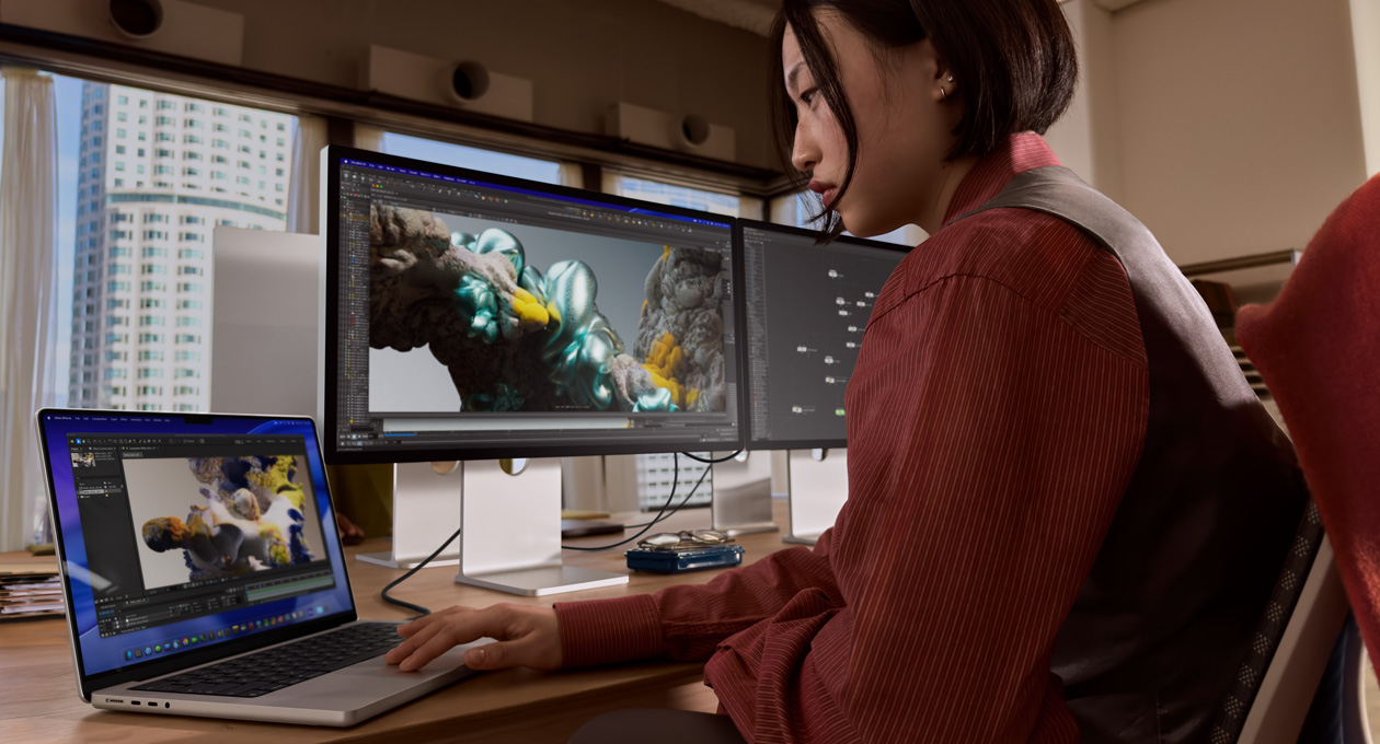 一個人在辦公環境中，使用 MacBook 手提電腦工作，MacBook 透過 Thunderbolt 5 連接埠連接至 Studio Display XDR